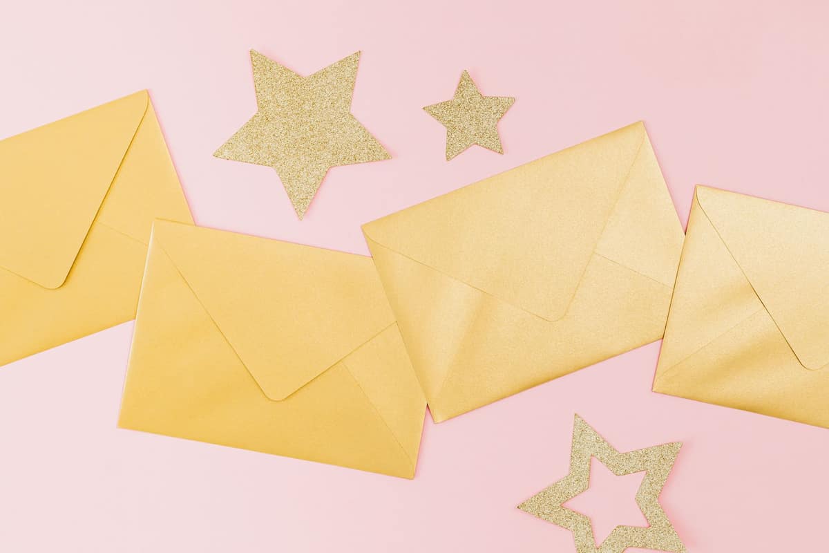 Golden envelopes and glittery stars on a pink background, perfect for festive celebrations.