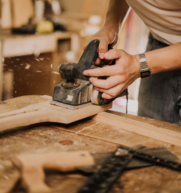 Hands planing a length of timber in a workshop, used as the backdrop of a sample reel script.